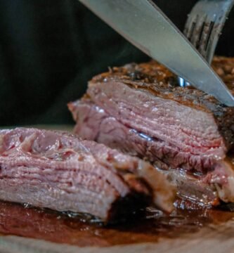 person slicing juicy medium rare meat on top of brown wooden cutting board