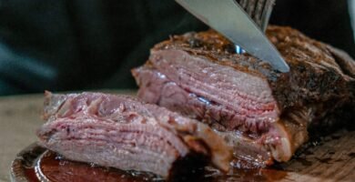 person slicing juicy medium rare meat on top of brown wooden cutting board